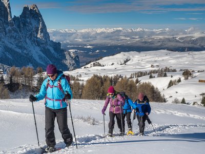 Snowshoeers ascending snowy hill with mountains in far distance on sunny day, St Zyprian, Italy