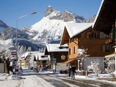 Kandersteg mountain village during winter with snow-covered building roofs and melted snow on roads with few people walking along them 