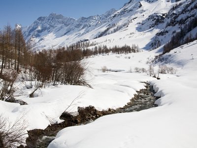 Lonza River in Switzerland during winter with snow covering landscape and tall mountains in distance in clear sunny blue sky day 