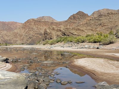 Landscape of mountains and low level body of water with smooth rocks scattered across and green shrubbery in background, South Africa