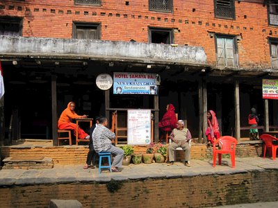 Outdoor scene of a restaurant named "Hotel Samaya Bai & Newa Khatta Gar" located at brick building. Several people are seated outside. Nepal