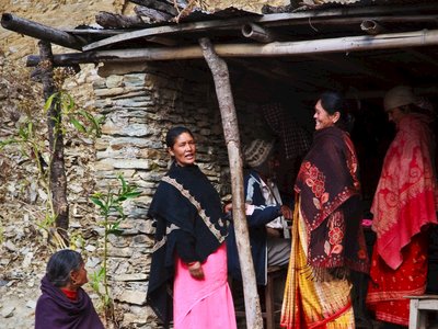 Group of women in traditional attire engage in conversation outside a rustic stone house, Nepal