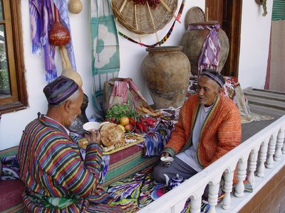 Elderly men leisurely enjoying tea while in conversation wearing colourful clothing and sat on detailed carpet, Uzbekistan