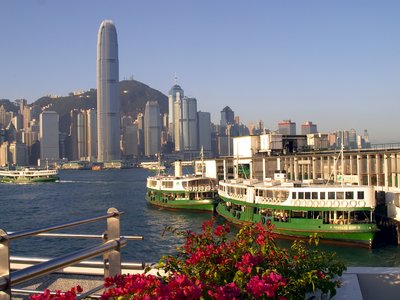 Star Ferry boats docked and leaving dock sailing towards Hong Kong cityscape in distance on sunny day
