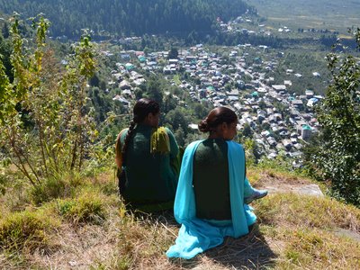 Two Indian women sat near grassy cliff edge admiring view of town, India