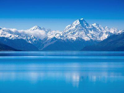 Lake Tekapo with snow-capped mountains in far distance with clear blue sky and still lake, South Island, New Zealand