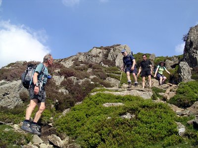 Man watching rest of hiking group carefully traverse down the rocks of Great Gable, Buttermere, Lake District, United Kingdom