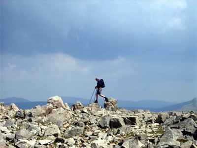 Distant side-angle view of man stepping from one rock to another atop Great Gable peak, Buttermere, Lake District