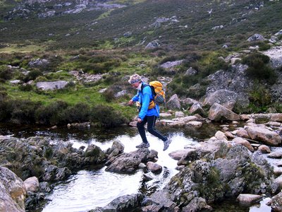 Lady stepping on rocks as she passes over body of water at Red Pike, Western Fells of Lake District - situated between Ennerdale from Buttermere Valley and Crummock Water
