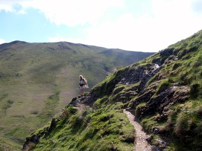 Woman rambling along mountainside path on edge of Sail hill in Buttermere in the Lake District on sunny day