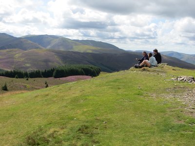 Three people sitting atop a grassy hill taking in the calming scenery of the Lake District