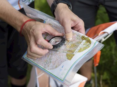 Hand holding compass on map to navigate route using orienteering skills