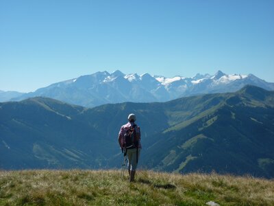 Man observing Hochkonig atop a grassy mountain on walking holiday, Maria Alm