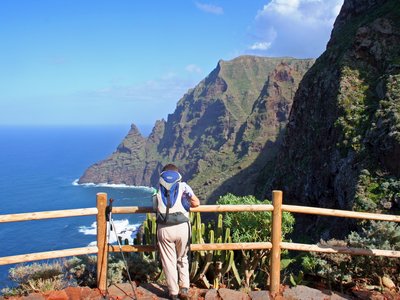 Male hiker leaning against wooden post admiring coastal landscape of Tenerife, Canary Islands, Spain