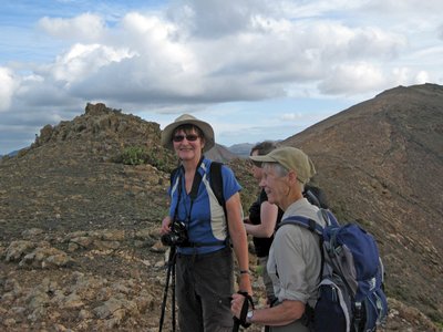 Small group of happy smiling walkers holding camera and trekking poles whilst standing atop rocky peak, Los Ajaches, Lanzarote, Canary Islands, Spain
