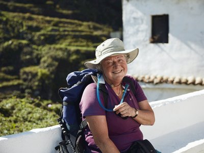 Lady on Ramble Worldwide walking holiday in La Gomera wearing walking gear resting by wall and smiling at camera whilst holding water tube, Canary Islands, Spain