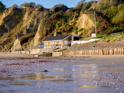 Beach house nestled by grassy cliffs viewed in distance across wet beach, Whitecliff Bay beach, Bembridge, Isle of Wight