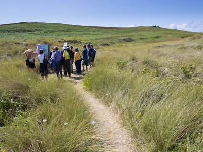 Ramble Worldwide walking group gathered around information point in grasslands, Isles of Scilly, England