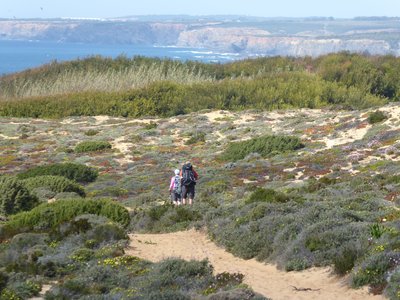Couple on Ramble Worldwide walking holiday walking along sandy coastal trail with low vegetation in Portugal near Atlantic sea