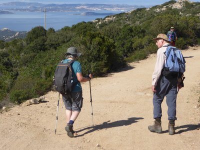 Walking enthusiast with walking poles walking alongside companion on dirt path on sunny day, Sardinia
