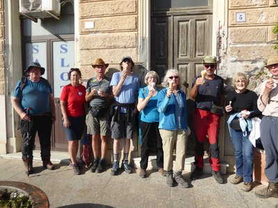 Group of walkers standing in front of building enjoying ice cream and posing for camera on sunny day, Sardinia