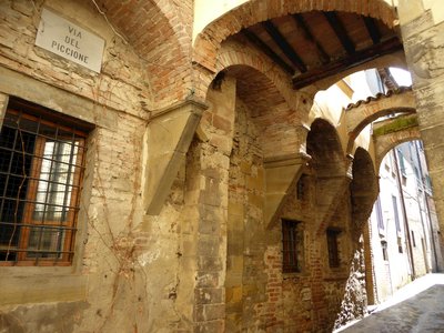 Città di Castello alleyway at via del piccione housing area, with brick arches joining buildings and sun shining through, Italy