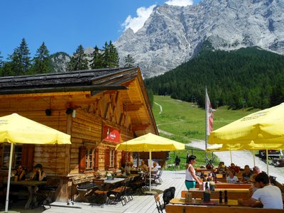 People seated at tables outside Gamsalm mountain cabin on sunny day, Ehrwald, Austria