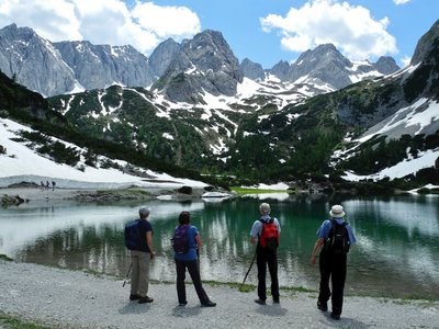 Four hikers admiring partially snow-covered Zugspitz mountain from Seebensee lake on sunny day, Austria