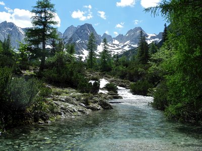 Clear light blue river running between pine trees with Zugspitz mountain in background, Austria