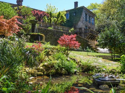 Colourful garden of various plants and water feature with old vine-covered brick building in background, historic landmark Faramello Palace, Pazo do Faramello, Spain