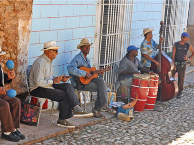 Group of Cuban street musicians playing various instruments in shadow of cobblestone street, Cuba, Caribbean