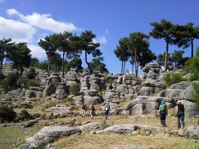 Walking group on St Paul Trail in Selge with interesting smooth rock formations and tall pine trees in distance, Turkey
