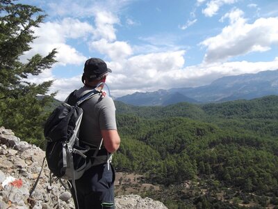 Hiker on Saint Paul Trail standing by cliff edge looking at mountains in distance beyond pine forest, Turkey