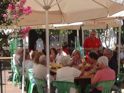 Group of people enjoying tapas whilst sat under parasol at outdoor restaurant