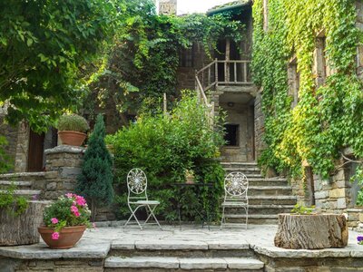 Saxonis House built from stone and green vines growing across walls with potted flowers on patio aside garden chairs, Papingo, Greece