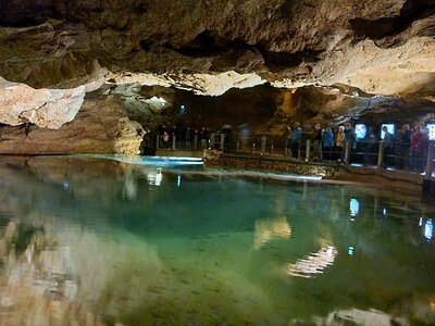 People on path around spotlighted green water with low-hanging rock ceiling within famous cave Gouffre de Padirac in France, Europe