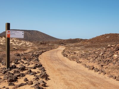 Los Lobos walking signpost positioned next to trail in arid rocky mountainous land showing direction and distance to beach and lighthouse, Fuerteventura, Canary Islands, Spain