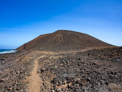 Rocky footpath leading to fork in road of volcanic landscape near sea, on the island of Lobos, Fuerteventura