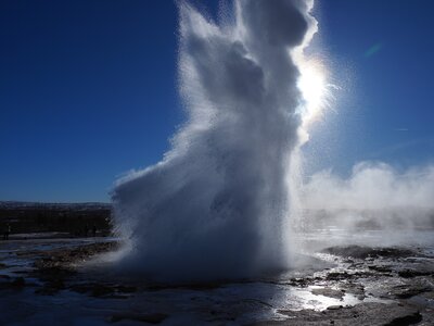 Geysir on Golden Circle with sun in background shining and highlighting fine mist, Iceland