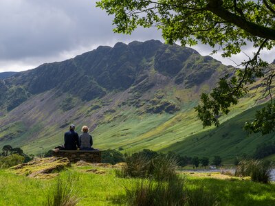 Couple sitting beneath oak tree admiring Haystacks, Lake District, England