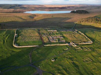 Aerial view of auxiliary fort remains extending from Hadrian's Wall in middle of a green field, Housesteads Roman Fort, Northumberland, England