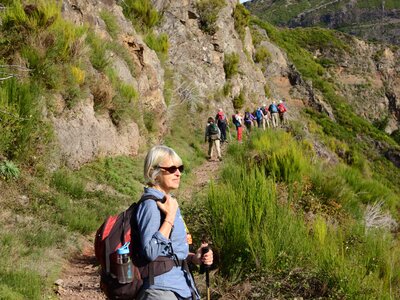 Side profile of lady on grassy mountain path taking in view with line of ramble worldwide walkers up ahead, Madeira, Portugal