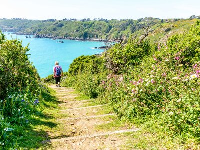 Female hiker descending stairs on pathway on sunny day, Guernsey