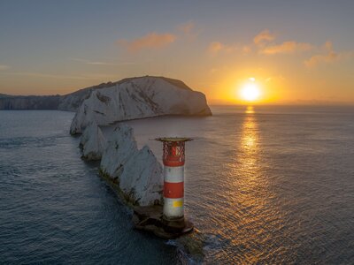 The Needles Isle with lighthouse in foreground and sunset casted from horizon leading golden glow across water past lighthouse, Isle of Wight, UK