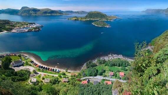 Seljesanden Beach with houses dotted along curve of coast and green islands in distance, Selje, Norway