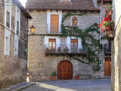 Hecho Valley Village Pyrenees Houses with red flowers growing on balconies and green vines growing freely on cobblestone bricks across houses, Spain