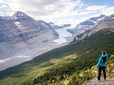 Hiker viewing Saskatchewan Glacier  in alpine valley and Castleguard Peak from above Parker Ridge, Canada