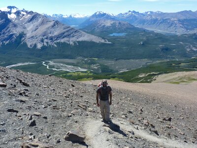 Front view of Ramble Worldwide walking holiday hiker ascending rocky hill with mountains in background, El Chalten, Patagonia