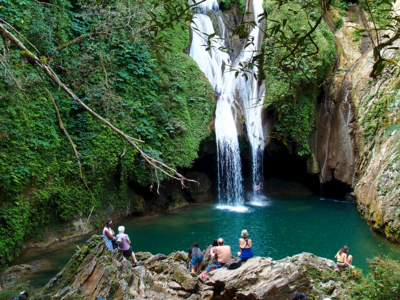 Gran Parque Natural Topes de Collantes, Cuba national park with large waterfall crashing into turquoise water and people sat on rocks admiring view from distance