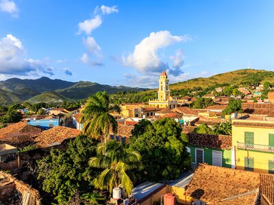 High view of Trinidad on sunny day with palm trees, church, and green mountains in distance, Cuba, Caribbean